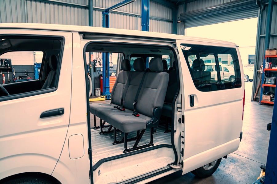 A van with its side door open showing a newly fitted row of passenger seats with seatbelts